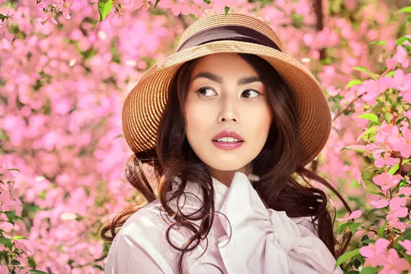 Güneşli bir gün ve mutlu bahar havası. Kadın güzelliği ve bahar. Güzel bir Asyalı kızın portresi. Etrafında çiçek açan sakuranın pembe çiçekleri var..