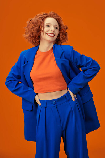 Summer Fashion. Portrait of beautiful cheerful redhead girl smiling laughing in bright blue and orange clothes. Bright colors. Studio orange background.