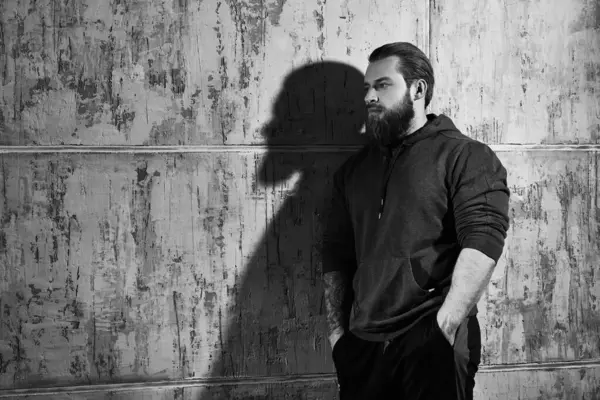 Büyük, güçlü bir adam beton bir duvara yaslanmış, düşüncelere dalmış. Siyah-beyaz bir portre. Mesaj için yer. Psikolojik resim.