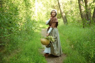 18. yüzyıl kostümü giymiş kırsal bir İskoç kızı güneşli ormanda gülümseyerek yürür. 18. yüzyılın tarihi yeniden yapılandırması. İskoç kız.