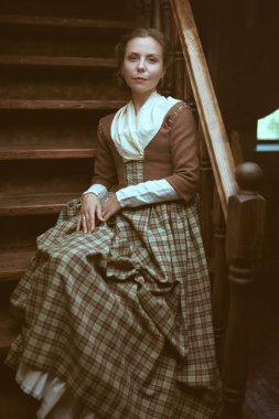 18. yüzyıl tarzı. 18. yüzyıldan kalma İskoç elbiseli güzel bir aristokrat kız klasik iç mimarisi olan bir odada merdivenlerde oturuyor. Romandaki kadın kahraman..