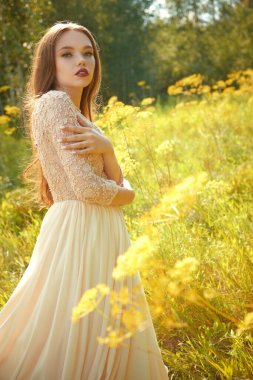 Muhteşem dantel elbiseli güzel bir kızın çekimi güneş ışığı altında yeşilliğin ortasında doğada duruyor. Yaz güzelliği ve moda. 