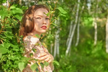 Yeşil yapraklarla çevrili ormanda narin bir kız duruyor. Yaz güzelliği ve makyajı.
