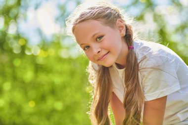 Mutlu yaz zamanları. Güneşli bir yaz gününde saçı örgülü şirin ve komik bir kızın portresi. Şaşkınlıkla kameraya bakıp gülümsüyor. Yaz tatili.