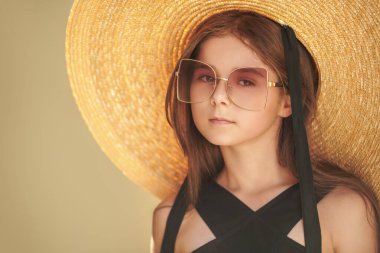 Şehir sokaklarında küçük bir moda düşkünü. Zarif, geniş kenarlı bir şapka ve güneşli bir yaz gününde açık havada moda olan güneş gözlüklü güzel bir kızın portresi. Çocuk modası.. 