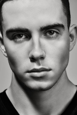 Kameraya ciddi ve kararlı bir şekilde bakan vahşi bir gencin siyah beyaz portresi. Erkeklik ve güzellik. Gri stüdyo geçmişi.