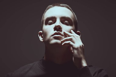 Koyu gri stüdyo arka planında kısa saç kesimi olan yakışıklı, şehvetli bir gencin koyu renkli portresi. Erkek güzeli..