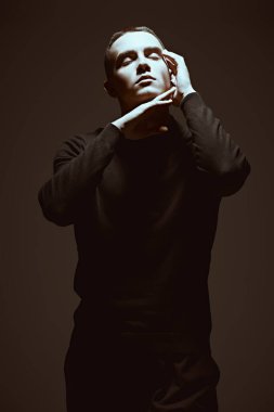 Erkeklerin psikolojisi. Siyah elbiseli genç bir adamın sanat portresi. Karanlıkta gözleri kapalı duran ve yüzünü aydınlatan bir ışık huzmesi. Siyah stüdyo geçmişi.