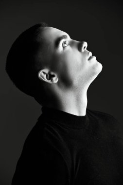 Kısa saçlı, siyah elbiseli, koyu gri bir stüdyo geçmişine bakan genç bir adamın portresi. Siyah beyaz portre. Bir adamın psikolojisi..