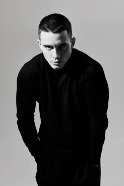 Kısa saçlı, siyah elbiseli, gri bir stüdyo arka planında poz veren vahşi bir gencin sanat portresi. Siyah beyaz portre. Bir adamın psikolojisi..