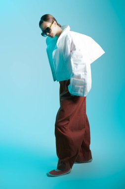 Mavi stüdyo arka planında tasarımcı kıyafetleriyle poz veren güzel bir manken kız. Moda özel tasarım koleksiyonu. Geniş serbest kıyafet, büyük boy stil. 