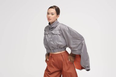 Yüksek moda. Güzel bir mankenin portresi şık gri bir ceket ve geniş kahverengi pantolonla beyaz stüdyo arka planında mesajlaşma yeri olan güzel bir manken. Gelecekçi Moda Biçimi. 