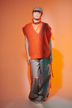 Yeni moda yarı sezon koleksiyonu. Tasarımcı örgüsü. Geniş paçalı pançoyla poz veren şık bir manken, atölyede örgü ören panço ve karışık renkli ışıkta örgü ören bir şapka. Parlak renkler.