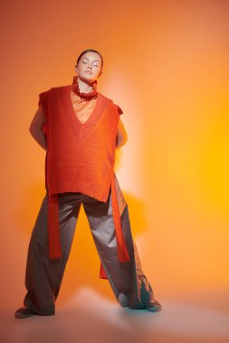 Yeni moda yarı sezon koleksiyonu. Tasarımcı örgüsü. Geniş paçalı pantolonla poz veren şık bir manken stüdyoda karışık renkli ışıkta panço örüyor. Parlak renkler.