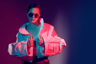 Moda ve moda tarzında. Güzel manken kız geniş şekilli şık kıyafetler içinde poz veriyor. Stüdyo karman çorman bir ışıkta koyu bir arkaplan karşısında. Parlak renkler. Boşluğu kopyala.