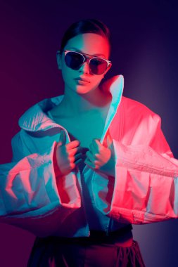 Güzel manken kız geniş şekilli şık kıyafetler içinde poz veriyor. Stüdyo karman çorman bir ışıkta koyu bir arkaplan karşısında. Parlak renkler. Moda ve moda modası.
