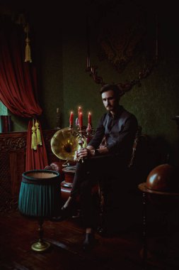 Klasik zengin yaşam tarzı. Yakışıklı, heybetli bir adam klasik iç mimarisi olan bir odada antika eşyalarla çevrili oturuyor. Erkek modası ve tarzı.