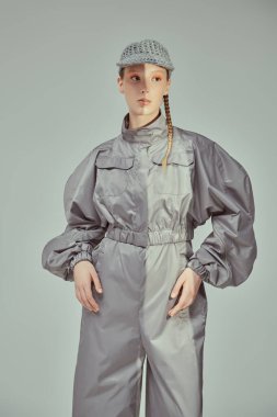 Yüksek moda. Gri bir takım elbise ve gri arka planda şık bir şapkayla poz veren güzel bir mankenin portresi. Gelecekçi Moda Biçimi. 