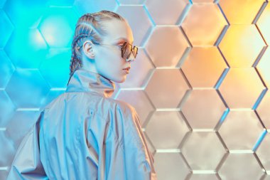 Fütürist moda tarzı. Gri bir takım elbise ve gümüş teknolojik arka planda şık güneş gözlüğü takan güzel bir mankenin portresi. Yüksek moda. Metin için yer.