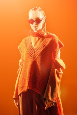 Yaz için özel tasarım koleksiyonu. Moda mankeni kız şık elmas şekilli gözlüklerle poz veriyor, turuncu bir bluz ve turuncu bir arka planda panço örüyor. Güneş gözlüğü için moda ve tarz.