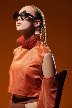 Yaz için özel tasarım koleksiyonu. Moda mankeni kız şık elmas şekilli gözlüklerle poz veriyor ve stüdyo arka planında turuncu bir bluz var. Güneş gözlüğü için moda ve tarz.