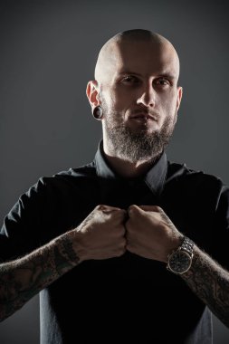 Gayri resmi, sakallı, vahşi görünümlü bir adam gri bir stüdyo geçmişine karşı poz veriyor..