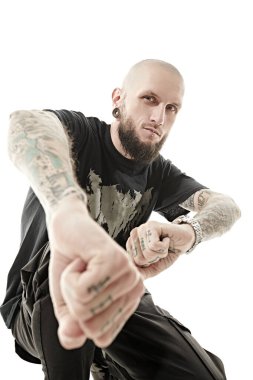 Gayri resmi görünüşlü, kafası tıraşlı, kulaklarında ve dudaklarında piercing olan, vücudunda dövmesi olan bir adam kameraya yumruklarını gösteriyor. Beyaz stüdyo geçmişi.