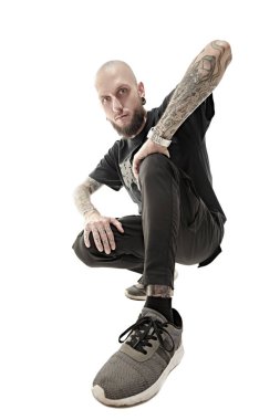 Gayri resmi görünüşlü, kafası kazınmış, dudağında ve kulaklarında piercing olan, vücudunda dövmesi olan bir adam stüdyoda siyah giysiler içinde poz veriyor. Beyaz stüdyo geçmişi. Rock müzisyeni.