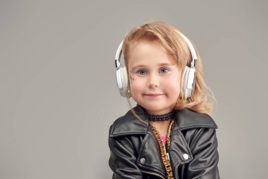 Parlak makyajlı, modaya uygun kıyafetleri ve aksesuarları olan sevimli bir kız ve rock müzisyeni kulaklıkla müzik dinliyor. Gri stüdyo geçmişi. Çocuk modası. DJ kız. Metin için yer.