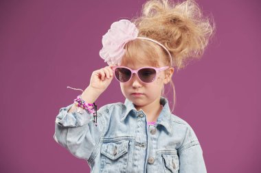 Kot ceketli, pembe güneş gözlüklü ve modaya uygun saç stili olan güzel bir moda kızı portresi. Stüdyo fuşya arka planı ve fotokopi alanı. Tatil.