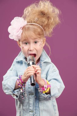 Şirin küçük kız. Şarkıcı mikrofonla şarkı söylüyor. Giysiler, aksesuarlar ve 80 'lerin tarzında saç stili. Parlak bir fuşya arka planına karşı stüdyo portresi.