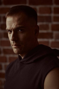 Erkekler, erkeklik ve güç. Siyah kapüşonlu güçlü bir adamın yakın plan portresi, odaklanmış ve yoğun bir şekilde kameraya bakıyor. Arka planda tuğla duvar var. Halk konsepti. 