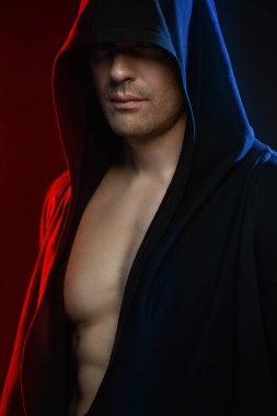 Boksör. Dövüşçü. Güçlü, atletik bir adam yüzünü bir kaputun altına saklayıp kameraya bakıyor. Stüdyo portresi ve karışık ışık. Güç sporları.