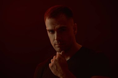 Güçlü ve kaslı bir adam kameraya titizlikle bakar. Karanlık bir arkaplanda, metin için yeri olan stüdyo portresi. İnsanlar ve duygular. Yaşam tarzı, seçimler. Spor..