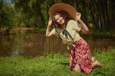 Güzel, romantik bir Asyalı kız, resimli bir yaz parkındaki göletin kıyısında duruyor. Mutlu ve huzurlu yaz havası. Yaz modası.