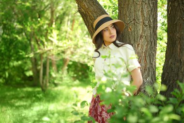 Yaz mutluluğu ve kaygısız ruh hali. Hasır şapkalı güzel bir Asyalı kız güneşli bir günde parkta yürüyor ve sıcak güneş ışınlarının tadını çıkarıyor..