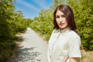 Mutlu güneşli günler. Güzel bir Asyalı genç kadın yemyeşil bir arka planda bir yaz parkının arka sokağında yürüyor. Yaz tatili.