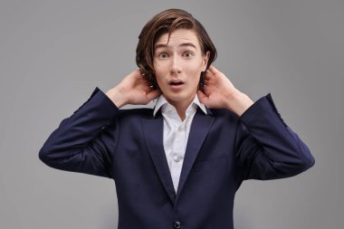 Modern eğitim. İnsanlar ve duygular. Klasik takım elbiseli bir gencin portresi. Şaşırtıcı ve heyecan verici. Gri stüdyo geçmişi.