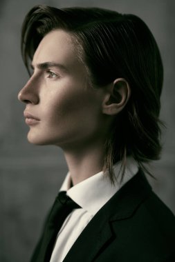 Moda ve tarz. Siyah şık klasik takım elbise, beyaz gömlek ve kravat giymiş şık saç modelli yakışıklı bir gencin profil portresi. Gri stüdyo geçmişi.