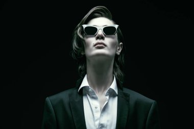 Erkek modası ve tarzı. Şık saç stili olan, zarif siyah klasik bir takım elbise, beyaz gömlek ve zarif güneş gözlüğü takan bakımlı bir gencin portresi. Kopyalama alanı olan siyah arkaplan. 