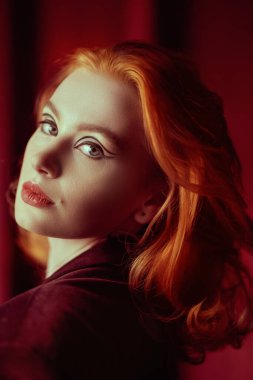 Kadın güzelliği ve tarzı. Pahalı kadife ceketli, loş ışıklı bir odada kızıl saçlı çekici bir genç kadın. Moda ve kadınlık. Oklarla ve saç stiliyle zarif bir makyaj..