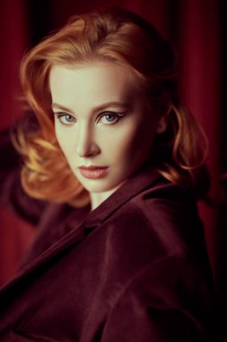 Kadın güzelliği ve tarzı. Pahalı kadife ceketli, loş ışıklı bir odada kızıl saçlı çekici bir genç kadın. Moda ve kadınlık. Oklarla ve saç stiliyle zarif bir makyaj..