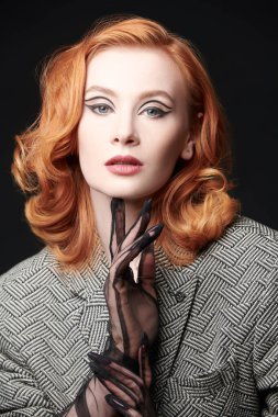 Siyah stüdyo arka planında ceketli, kızıl saçlı çekici bir kadının portresi. Zarif oklarla makyaj yapın. Hollywood dalgası saç stili. Zarif retro tarzı ve modası. 