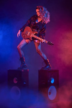 Konser. Etkileyici rock yıldızı kız, müzik hoparlörlerinin üzerinde gitar çalıyor. Rock müziği. Glam rock tarzı.