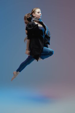 Dans ediyor. Gündelik giysiler içindeki güzel profesyonel dansçı kadın dans sırasında yüksekten atlıyor. Stüdyo tam boy portre.