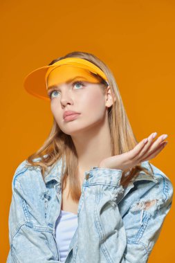 Denim gençlik tarzı. Kot ceketli güzel sarışın bir kızın portresi ve sarı bir stüdyo arka planında şık sarı bir güneşlik. Yaz modası. Spor kıyafetleri..