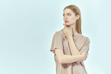 Beyaz stüdyo arka planında bej tişörtü olan güzel sarışın bir kız. İnsanların, yüzlerin ve duyguların konsepti. Metin için yer.