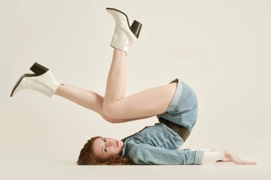 Denim Fashion. Kot pantolon ve beyaz deri botlarla beyaz stüdyo arka planında poz veren güzel, seksi bir genç kadının tam boy portresi. Güzellik ve özgüven.