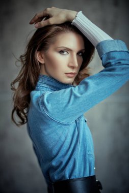 Gri arka planda kot gömlekle poz veren güzel kahverengi dalgalı saçlı çekici bir kızın portresi. Denim tarzı. Güzellik ve özgüven. 