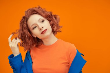 Parlak mavi ve turuncu elbiseli güzel kızıl saçlı kızın portresi. Parlak renkler. Stüdyo turuncu arka plan. Yaz Moda ve Tarzı.